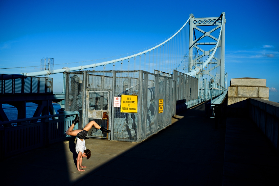 A woman does a handstand in a pocket of light on the ben franklin bridge.